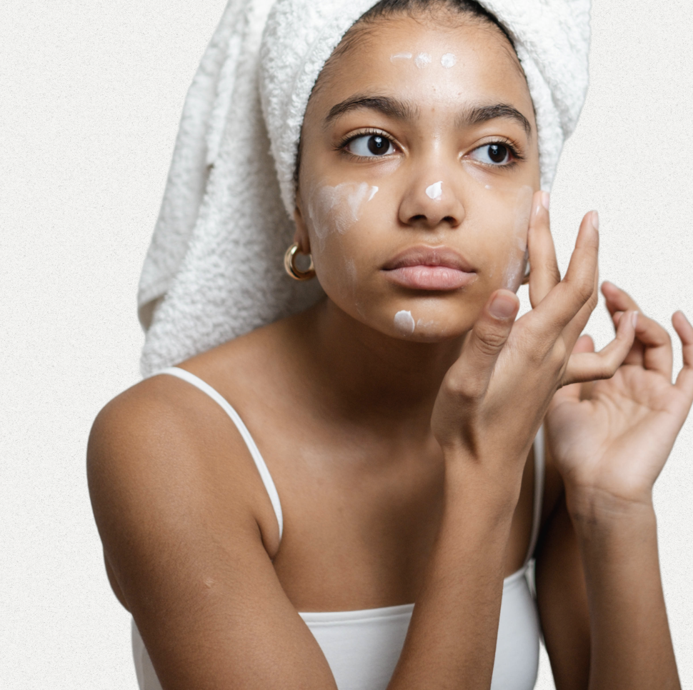 Person i 20–30-årsåldern som applicerar hudvård före spegeln, fokus på förebyggande anti-aging och solskydd.